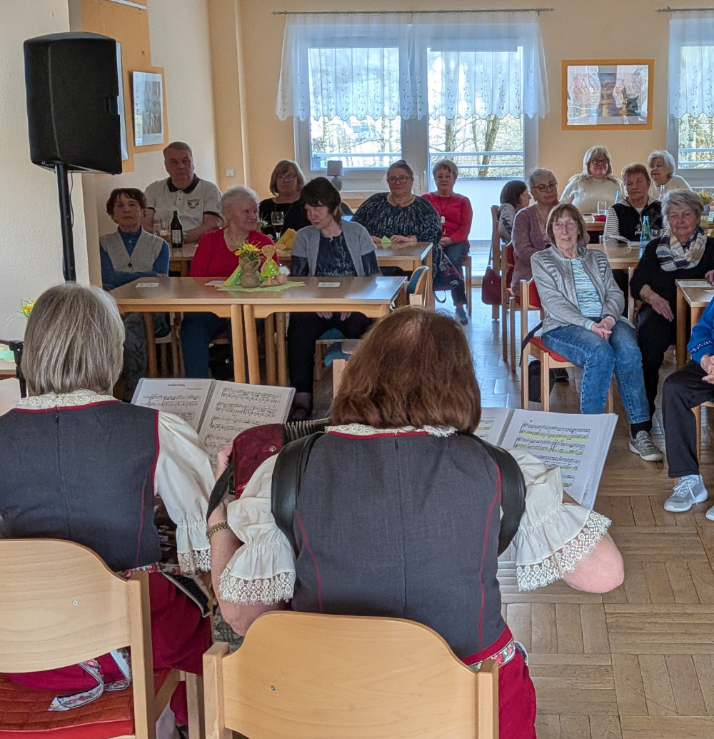 Viele Zuhörer:innen sitzen an Tischen und hören den beiden Musikerinnen zu.